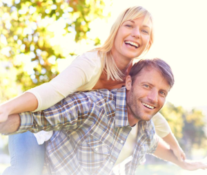 A woman and man laugh and smile, the woman balancing on the man's back in a fun pose