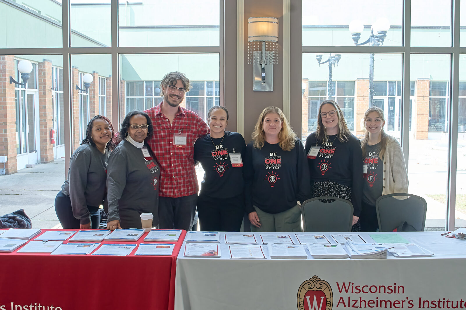 People wearing matching "Be one of 200" t-shirts stand behind a conference table