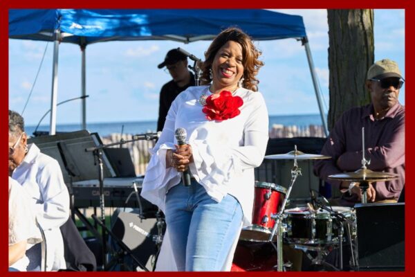 Woman smiles and holds microphone on a stage in front of a lake