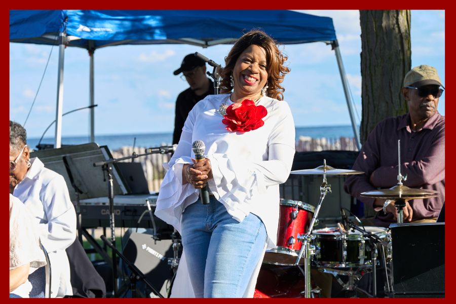 Woman smiles and holds microphone on a stage in front of a lake
