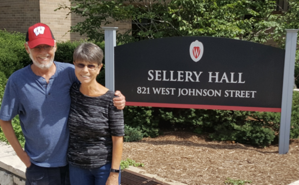 Couple stands with their arms around each other and smiling. The sign for UW dorm Sellery Hall is behind them. 